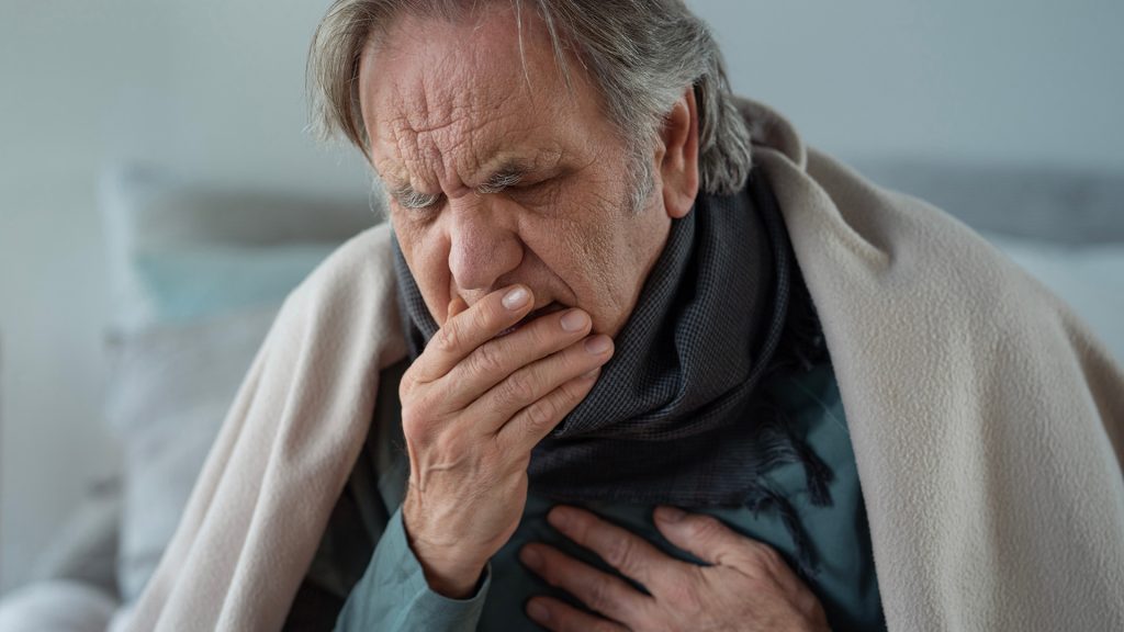 Elderly man coughing and holding his chest, indicating health issues from poor air quality.