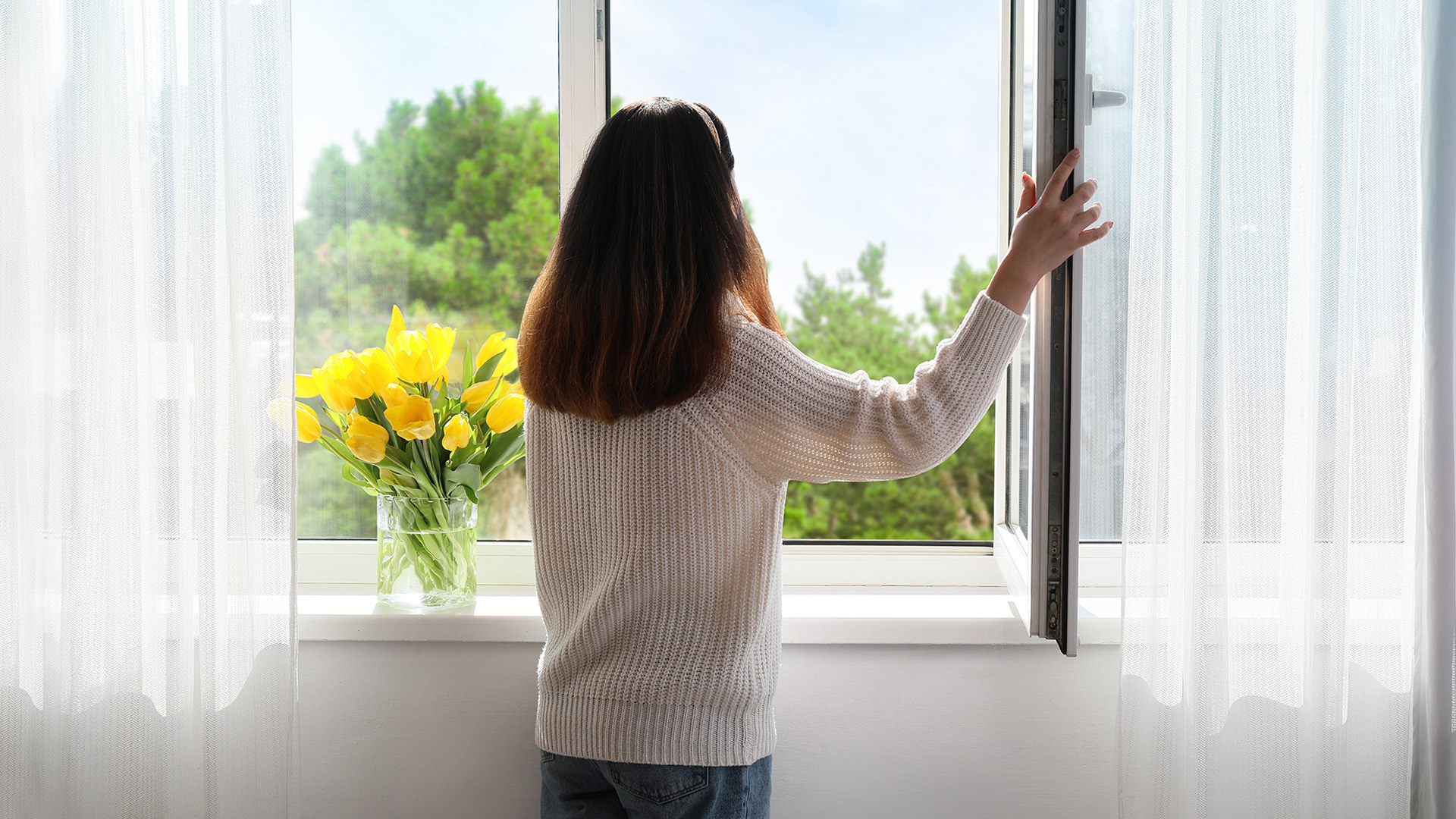 Woman opening a window to let fresh air into the house and remove odors.
